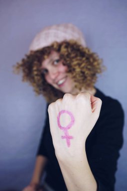 Yandan sembolünü gösterirken arka plan üzerinde pembe şapkalı kıvırcık saçlı sarışın genç kadın portresi