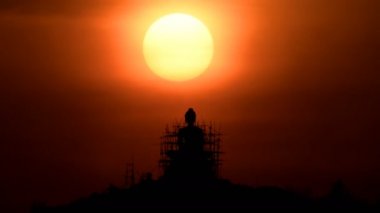 Time Lapse of sun and Buddha statue on mountain at sunset.