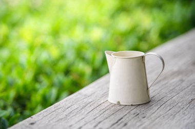 Bahçedeki ahşap masada beyaz çinko sürahi.