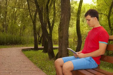 Bankta yazlık parkta oturan adam e-kitap okuyor