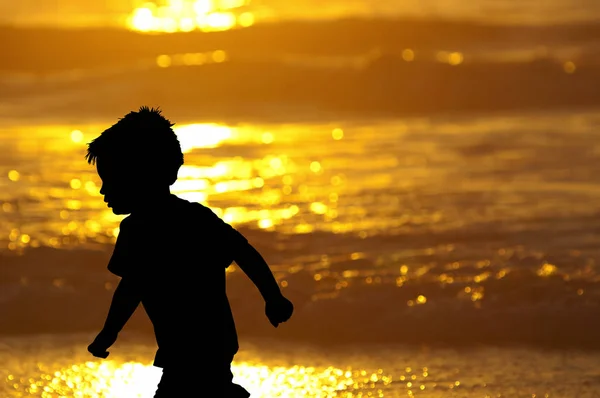 Маленький мальчик бегает вдоль пляжа на закате силуэт — стоковое фото