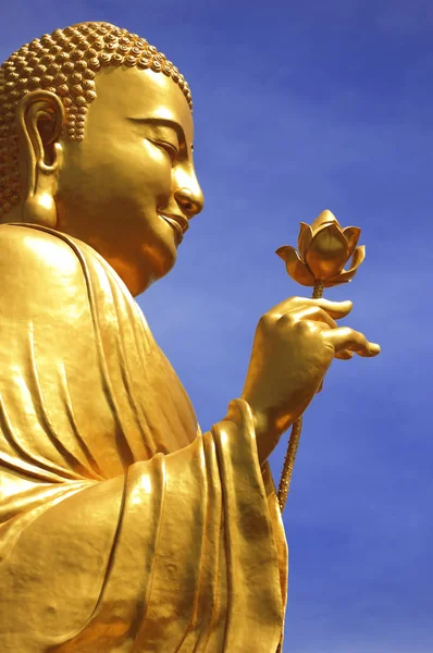 Estátua de Buda Dourado com mão segurando flor em um fundo azul céu (Da Lat, Vietnã ) — Fotografia de Stock