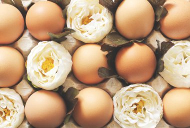 Tahta arka planda bir tepside yumurta ve çiçekler.