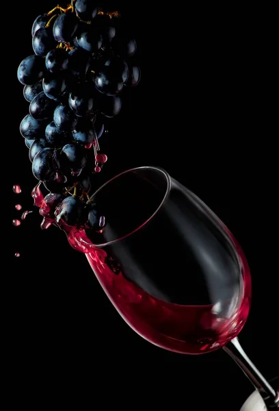 Vino rosso. Schizzi di uva scorrono in un bicchiere su fondo nero.. Isolati su fondo nero. Design artistico di confine Fotografia Stock