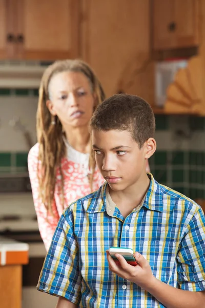 Mamma ser frågande som sonen tonåring kontrollerar sin telefon — Stockfoto