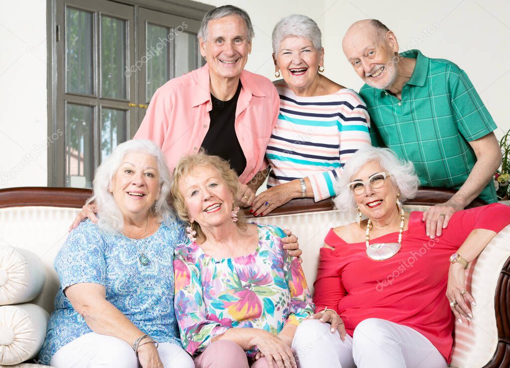 Six cheerful senior friends around an antique couch