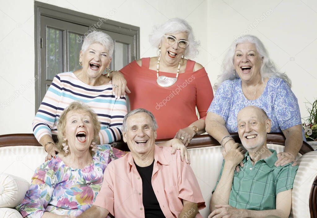 Six senior friends laughing out loud around an antique couch