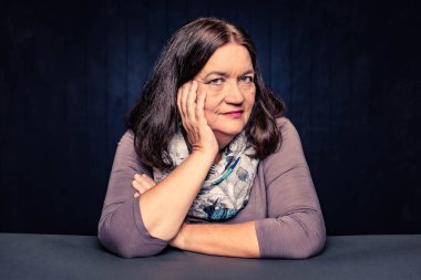 Yüzünde eli olan gülümseyen olgun bir kadının portresi.