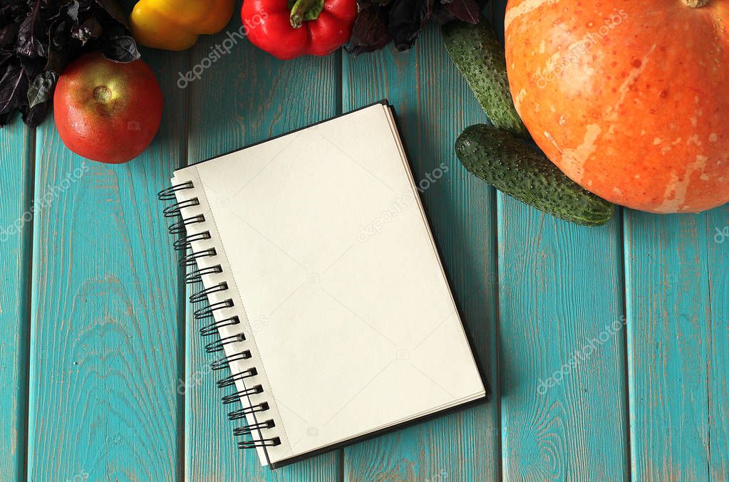 Note book and composition of vegetables on blue wooden desk.