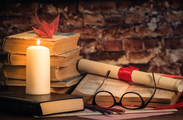Bir yığın kitap, açılış kitap, gözlük, mum, origami, kaydırma bir tuğla duvara ahşap masa üzerinde kırmızı kurdele ile bağlanmış