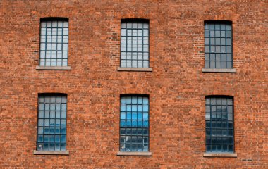 Bir sürü klasik pencereli kırmızı tuğladan yapılmış eski bir fabrika binasının önünde.