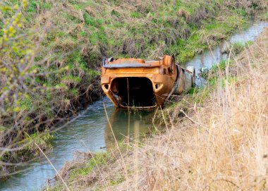 Eski paslı araba tarlalar arasında bir nehirde / bir derede, çevreyi kirletiyor.  