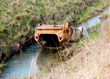 Eski paslı araba tarlalar arasında bir nehirde / bir derede, çevreyi kirletiyor.  