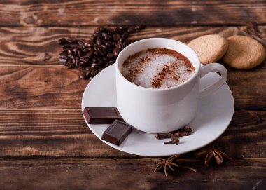 Köpüklü kahve, kek, kalp şeklinde kahve çekirdekleri ve ahşap masada çikolata. İnsansız Düz Yat