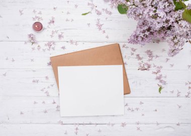 Bir el işi zarf, üzerinde beyaz kağıt, eski beyaz ahşap arka planda leylak ve mor mum.