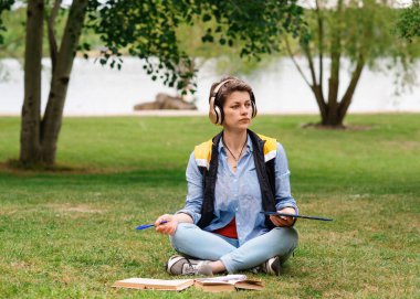 Yeşil çimlerin üzerinde oturan ve tablette internetten okuyan kadın.