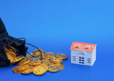 Siyah bir çantadan dökülen para ve mavi arka planda bir oyuncak ev