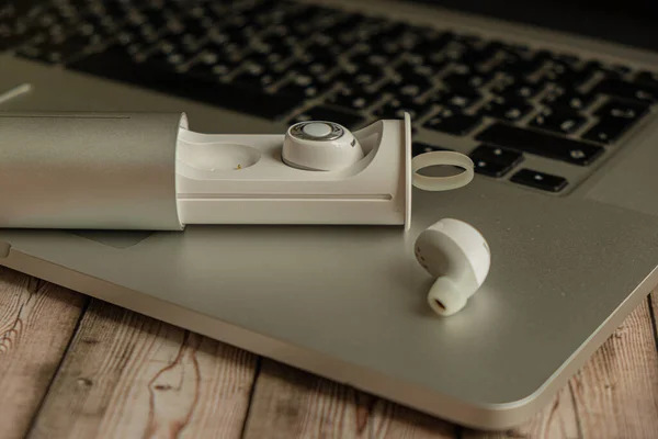 White wireless headphones charging case and laptop on a wooden background close-up, no body