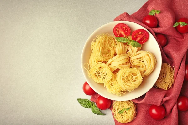 Tigela com ninhos de macarrão e tomate cereja na mesa — Fotografia de Stock