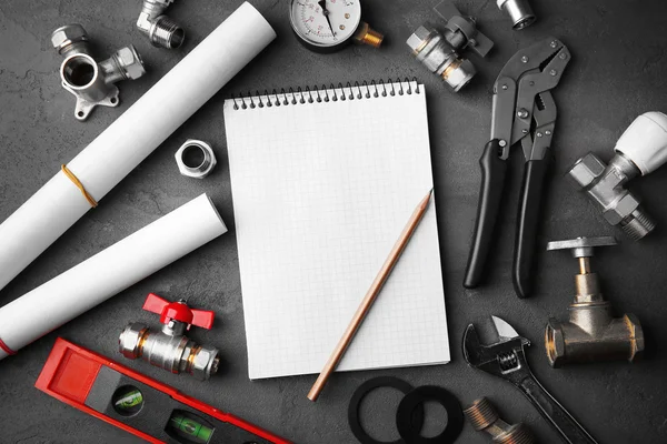 Notebook and plumber tools with blueprints on concrete structure background — Φωτογραφία Αρχείου