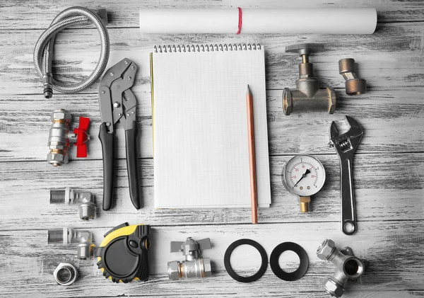 Herramientas de fontanero con cuaderno sobre fondo texturizado de madera — Foto de Stock