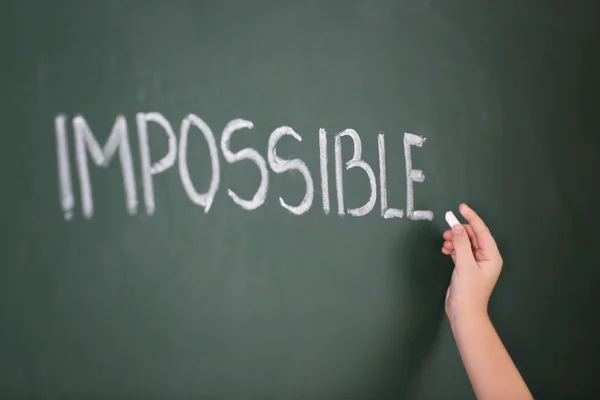 Little girl writing word impossible on chalkboard — Stock Photo, Image