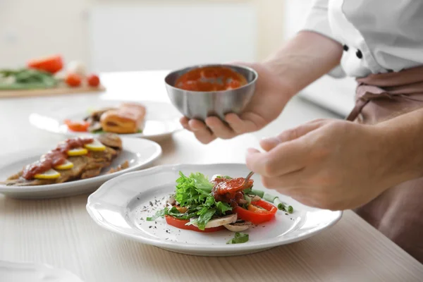 Jonge chef-kok koken zetten tomatensaus op gerechten — Stockfoto