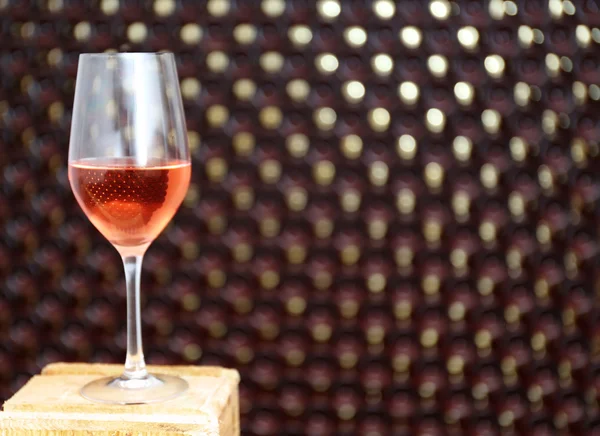 Glas wijn op wazig flessen muur achtergrond — Stockfoto