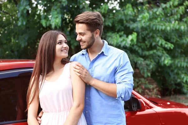 Bonito jovem casal de pé perto de carro vermelho — Fotografia de Stock