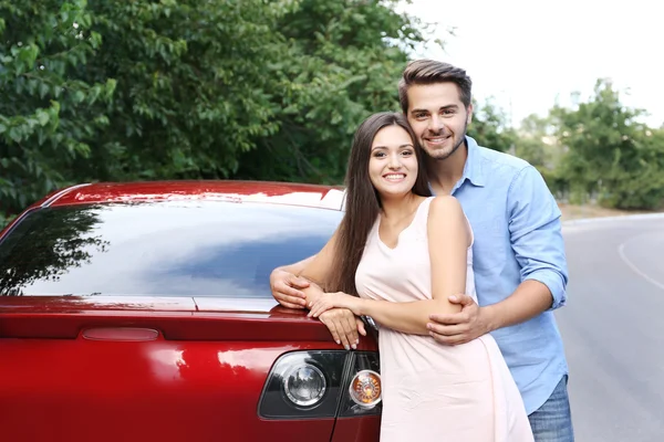 Kırmızı araba yakınındaki güzel genç çift ayakta — Stok fotoğraf