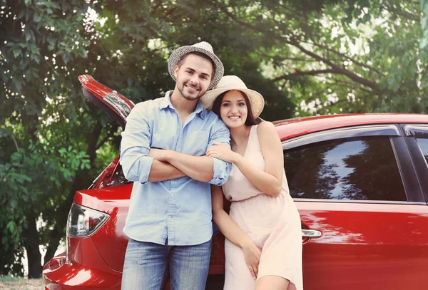 Hermosa pareja joven de pie cerca de coche rojo — Foto de Stock