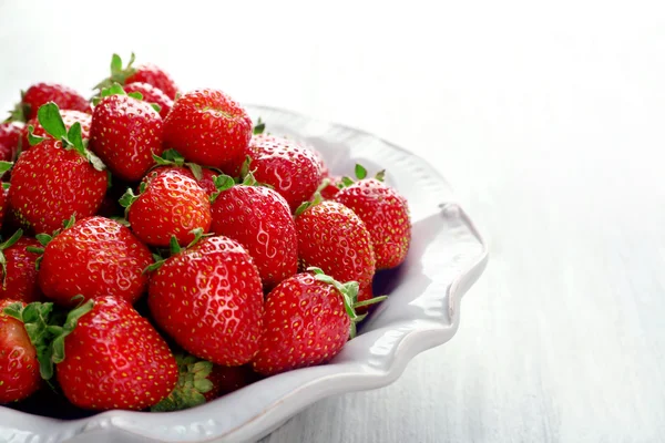 Assiette avec fraises juteuses sur fond de bois blanc — Photo