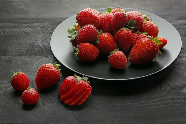 Black plate with ripe strawberries on dark wooden background — Stock Photo, Image