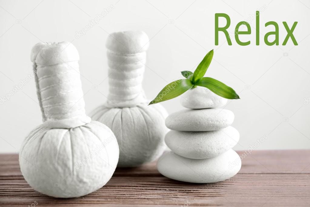 Spa composition with white stones and herbal massage stamps on wooden table. Word RELAX on light background.