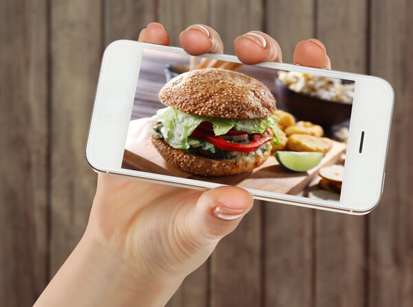 Female hand holding smartphone on blurred wooden background. Photo of food on smartphone screen.