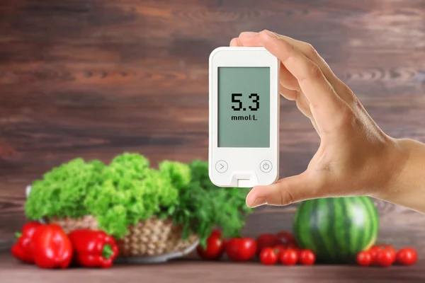 Male hand holding glucometer with fresh vegetables and greens on wooden background. Diabetes concept — Stock fotografie