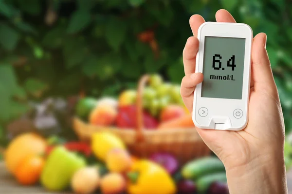 Male hand holding glucometer with fresh fruits and vegetables on table outdoors. Diabetes concept — Stock fotografie