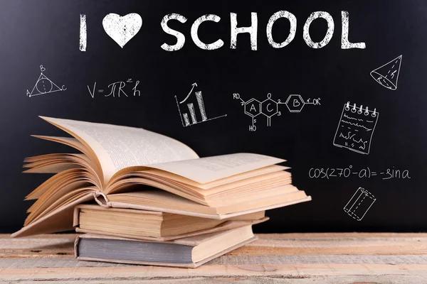 Stack of books on wooden table. Text I LOVE SCHOOL and icons on blurred blackboard background. Knowledge concept. — Stock fotografie