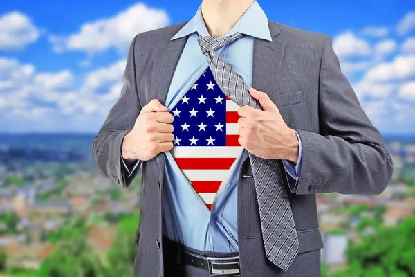 Businessman showing USA flag under suit on blurred cityscape background. — Stockfoto