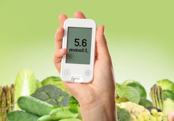 Männliche Hand hält Glukometer mit Gemüse und Obst auf grünem Hintergrund. Diabetes-Konzept — Stockfoto