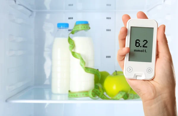 Männliche Hand hält Glukometer mit Lebensmitteln im Regal des Kühlschranks Hintergrund. Diabetes-Konzept — Stockfoto