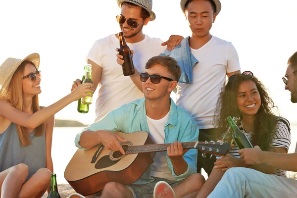 ギターを聴くと ビーチでビールを飲む友人のグループ — ストック写真
