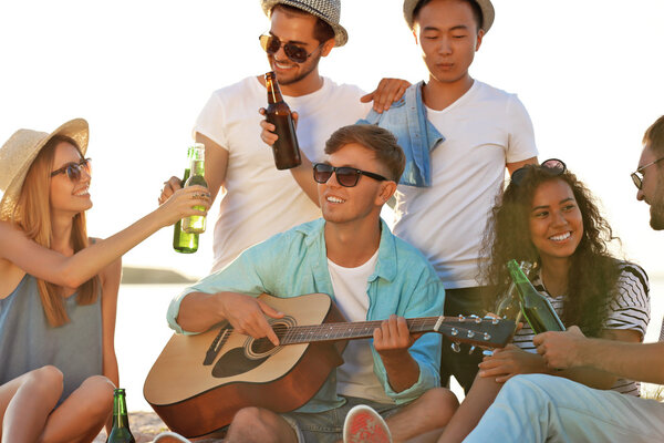 Group of friends listening to guitar and drinking beer at beach