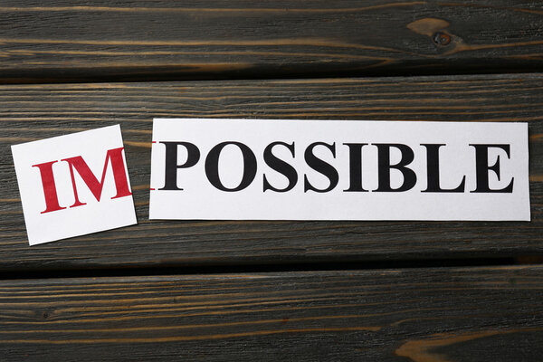 Cut out word IMPOSSIBLE on wooden background