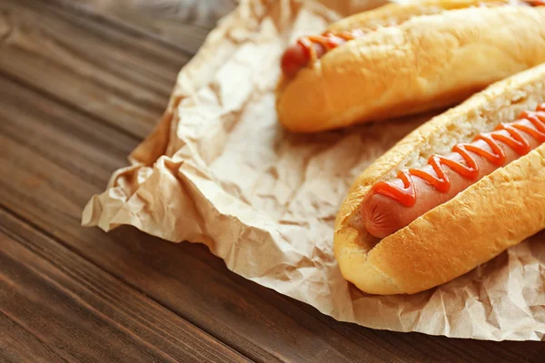 Gustosi hot dog su carta su sfondo di legno — Foto Stock