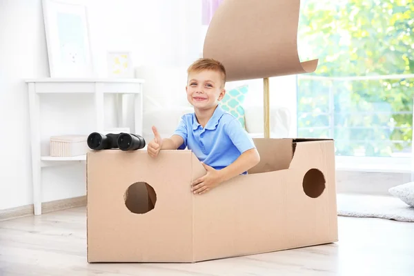 Мальчик играет с картонным кораблем в помещении — стоковое фото