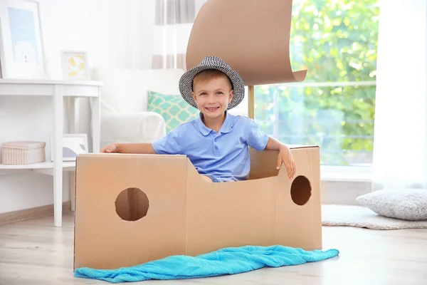 Мальчик играет с картонным кораблем в помещении — стоковое фото