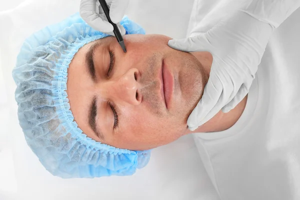 Koncepcja chirurgii plastycznej. Ręce w rękawiczkach, znakowanie męskiej twarzy — Zdjęcie stockowe