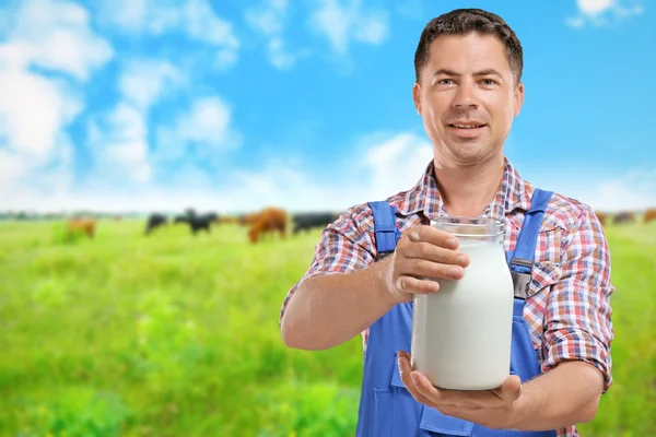 Handsome milkman with glass jar of milk on blurred cow pasture background. Dairy product concept. — Stock Photo, Image