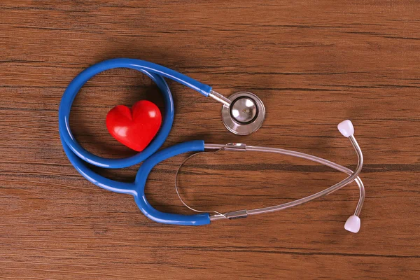 Stethoskop und rotes Herz auf Holztisch — Stockfoto